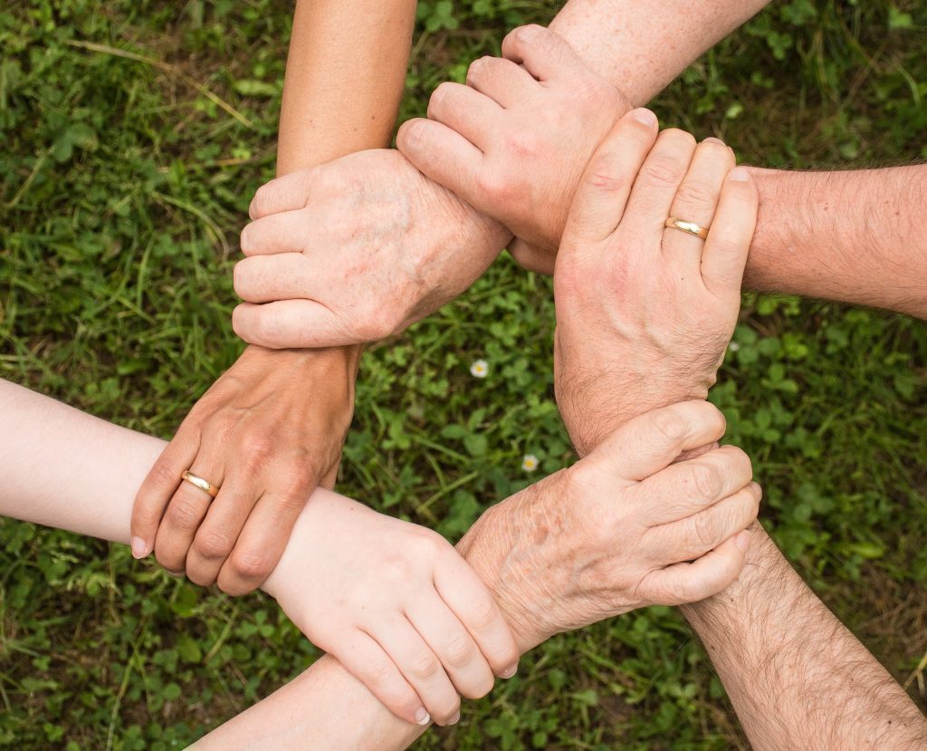 Several hands of different ages clasped together in a circle, symbolizing teamwork and unity.