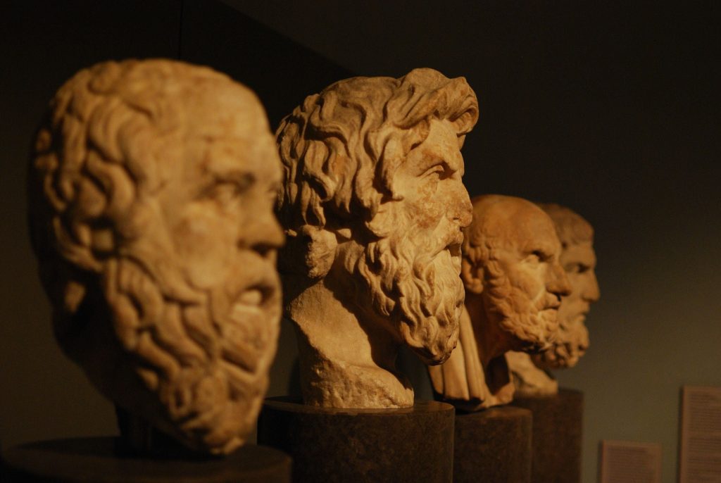 Row of ancient marble busts on display pedestals, lit from the side in a dark museum.