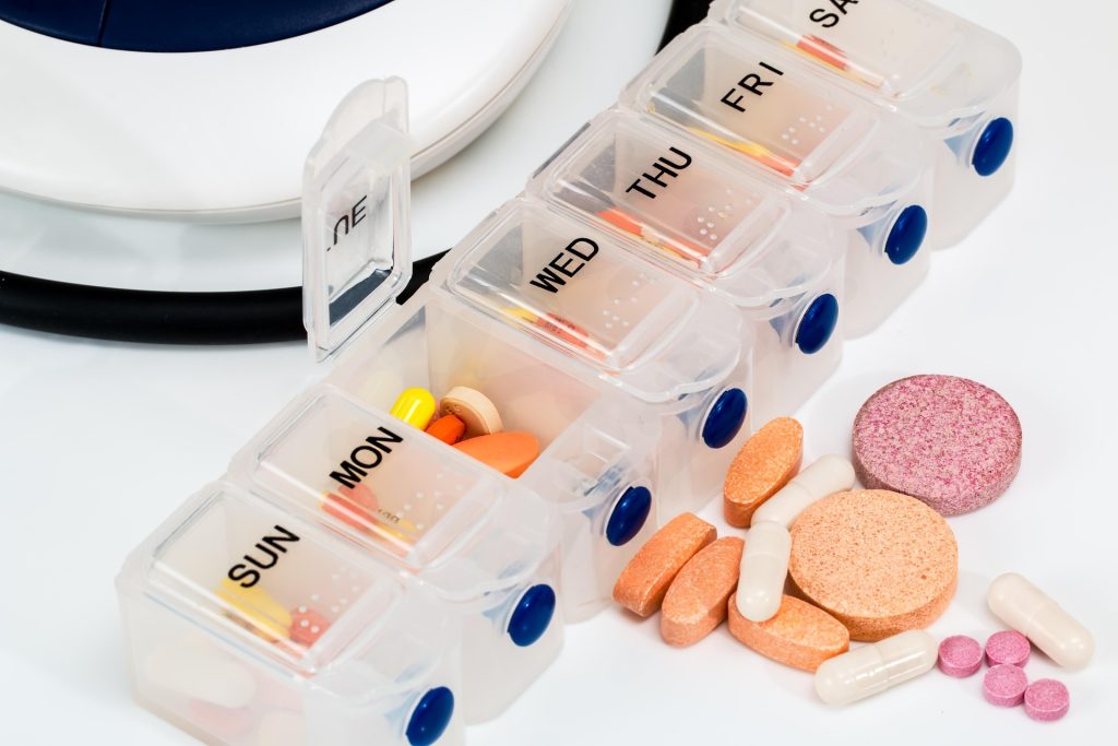 Open weekly pill organizer with days labeled Sun–Fri and scattered colorful pills nearby on a white surface.