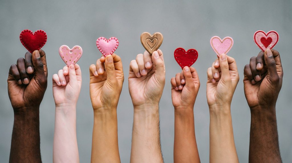 Diverse hands hold colorful fabric hearts in a row, symbolizing love and unity.